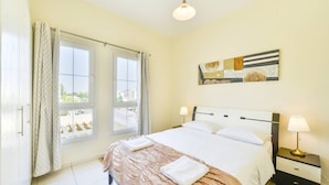 A hotel room with a bed, two bedside tables, a nightstand, a window with curtains, and a wall-mounted artwork. - Medlock Villas (Dubai)