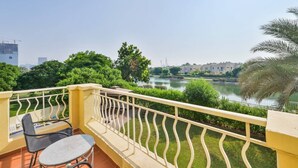 A balcony with a table and chairs, overlooking a river and greenery. - Medlock Villas (Dubai)