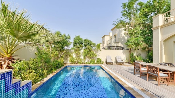 A rectangular swimming pool with blue tiles, surrounded by greenery and a wooden deck with chairs. - Medlock Villas (Dubai)