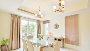 A dining area with a glass table, beige chairs, a potted plant, and a chandelier. - Medlock Villas (Dubai)