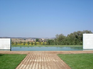A swimming pool with a wooden deck in the foreground and a view of a bridge and hills in the background. - Pago Del Vicario (Ciudad Real)