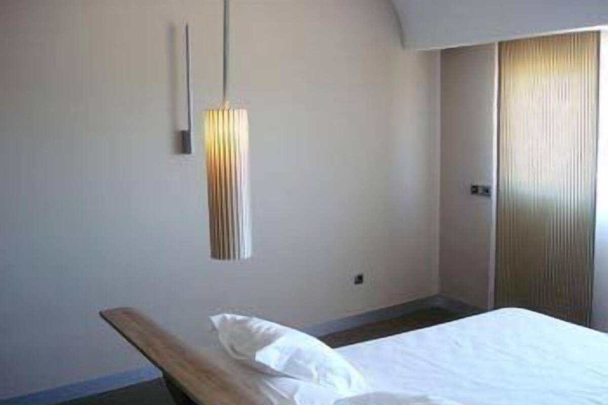 Et hotelværelse med en seng, et natbord, en lampe monteret på væggen og en dør.