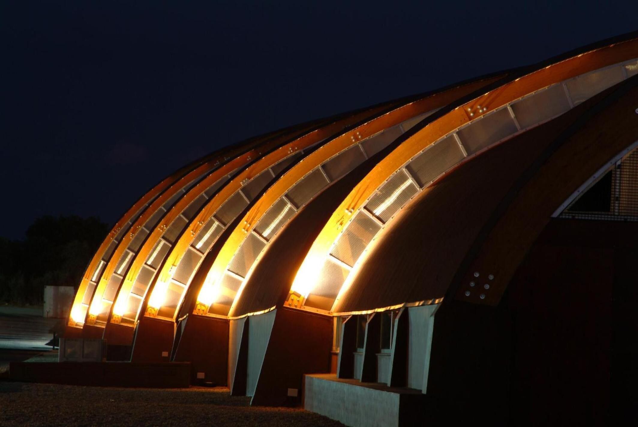 Un bâtiment moderne doté d’une structure de toit incurvée et de panneaux intérieurs éclairés.