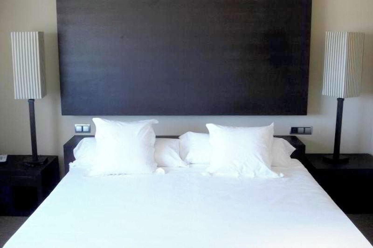 A hotel room with a large bed, two bedside tables, and two lamps.