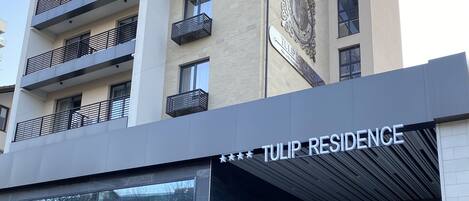 A modern building with a sign reading "TULIP RESIDENCE". It features a large glass entrance, multiple balconies, and a decorative emblem on the facade.