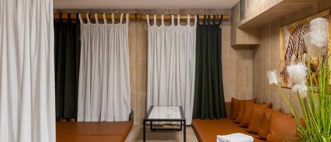 A modern spa room with a seating area, a table, and a large window with curtains.