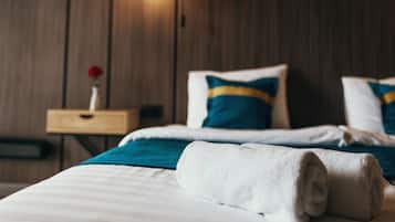 Un lit bien fait, avec une serviette blanche roulée, un oreiller aux tons turquoise et bleu, et une tête de lit en bois.