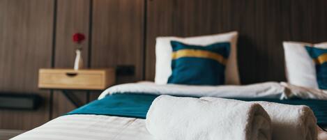 A neatly made bed with a rolled white towel, a teal and blue pillow, and a wooden headboard.