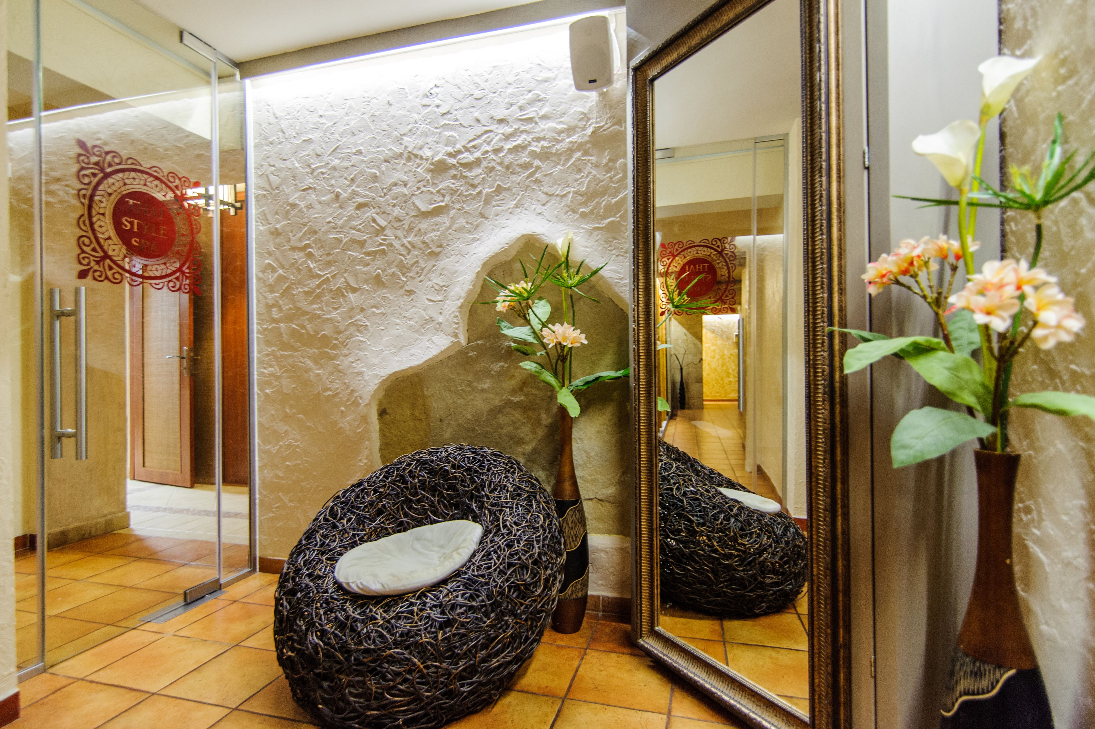 A spa room with a textured wall, a stone bench, a vase with flowers, and a mirror reflecting the room.