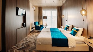 Una habitación de hotel moderna con una cama grande, un escritorio, una silla, un televisor y vistas de la ciudad a través de amplios ventanales.