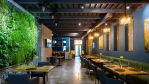 Un restaurante con una larga mesa de madera y sillas, un banco con cojín verde y una pared con plantas.