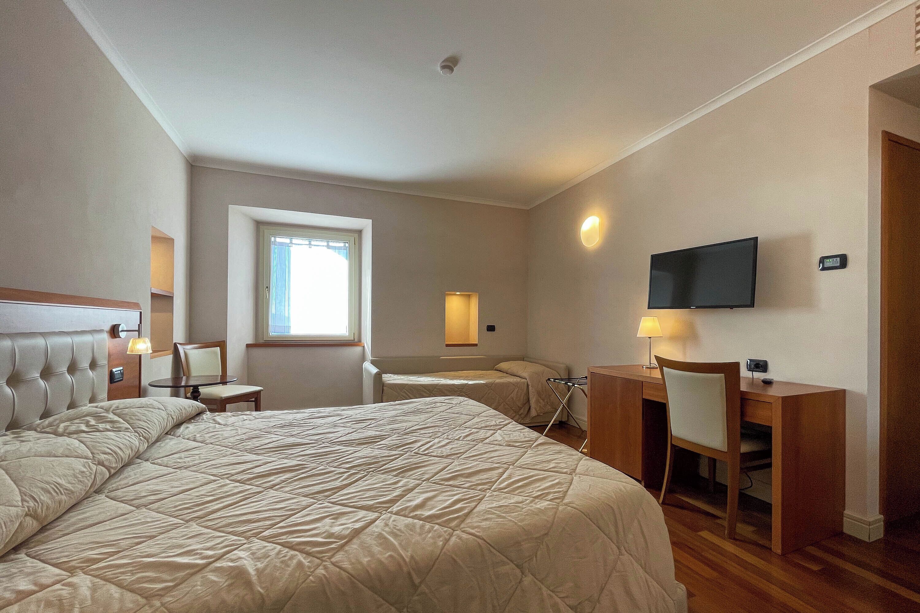 Una habitación de hotel con una cama grande, un escritorio, una silla, un televisor y una ventana.