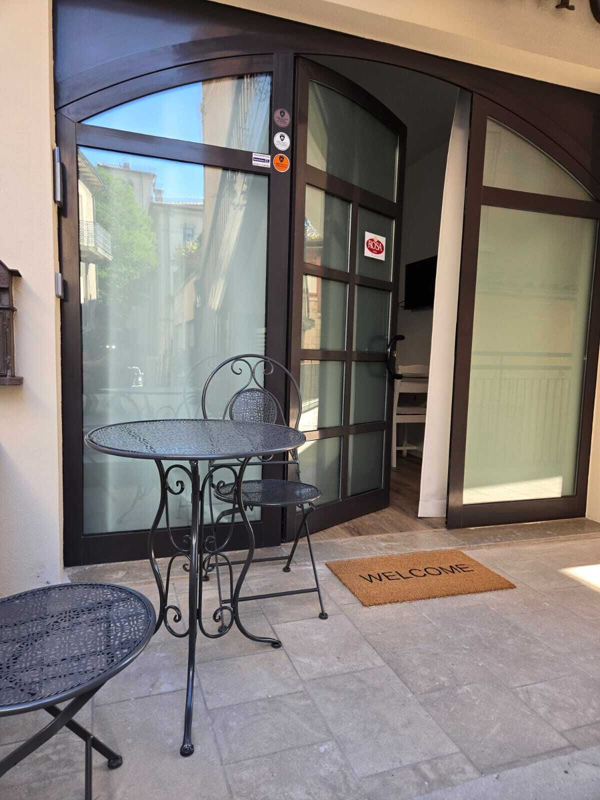 A patio area with two metal tables and chairs, a welcome mat, and a glass door with a sticker.
