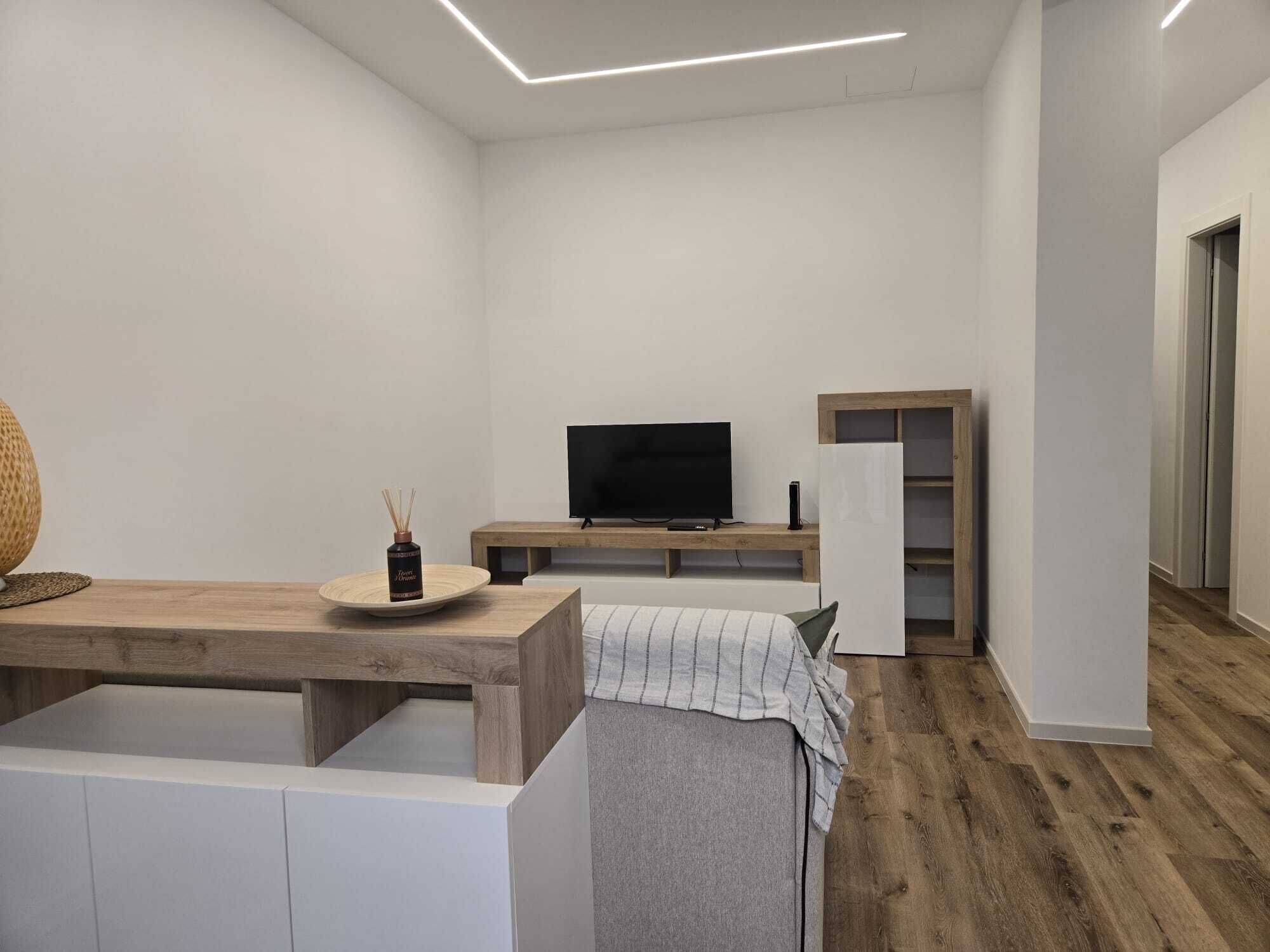 A modern, minimalistic living space with a flat-screen TV, a wooden coffee table, and a built-in bench.