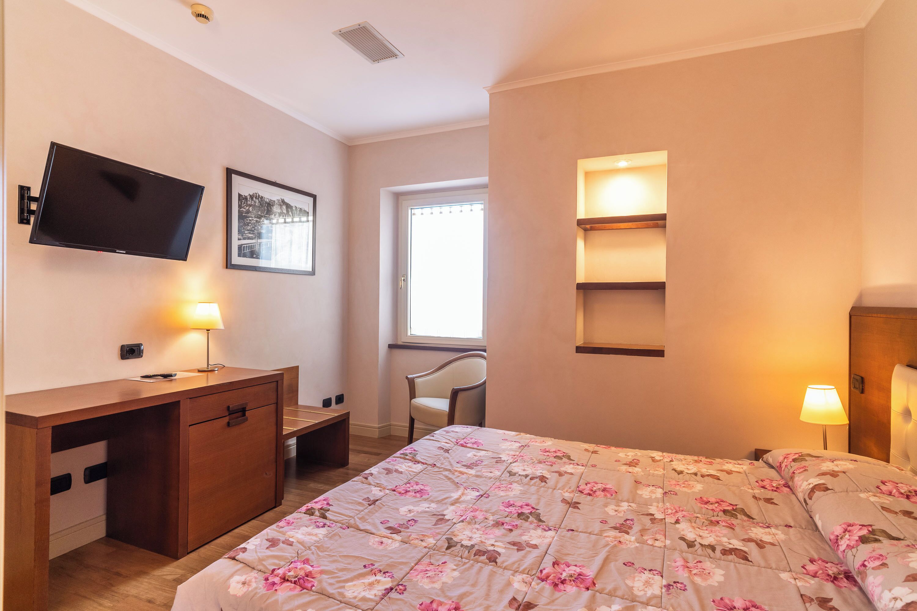 A hotel room with a bed, a desk, a chair, a TV, and a window.