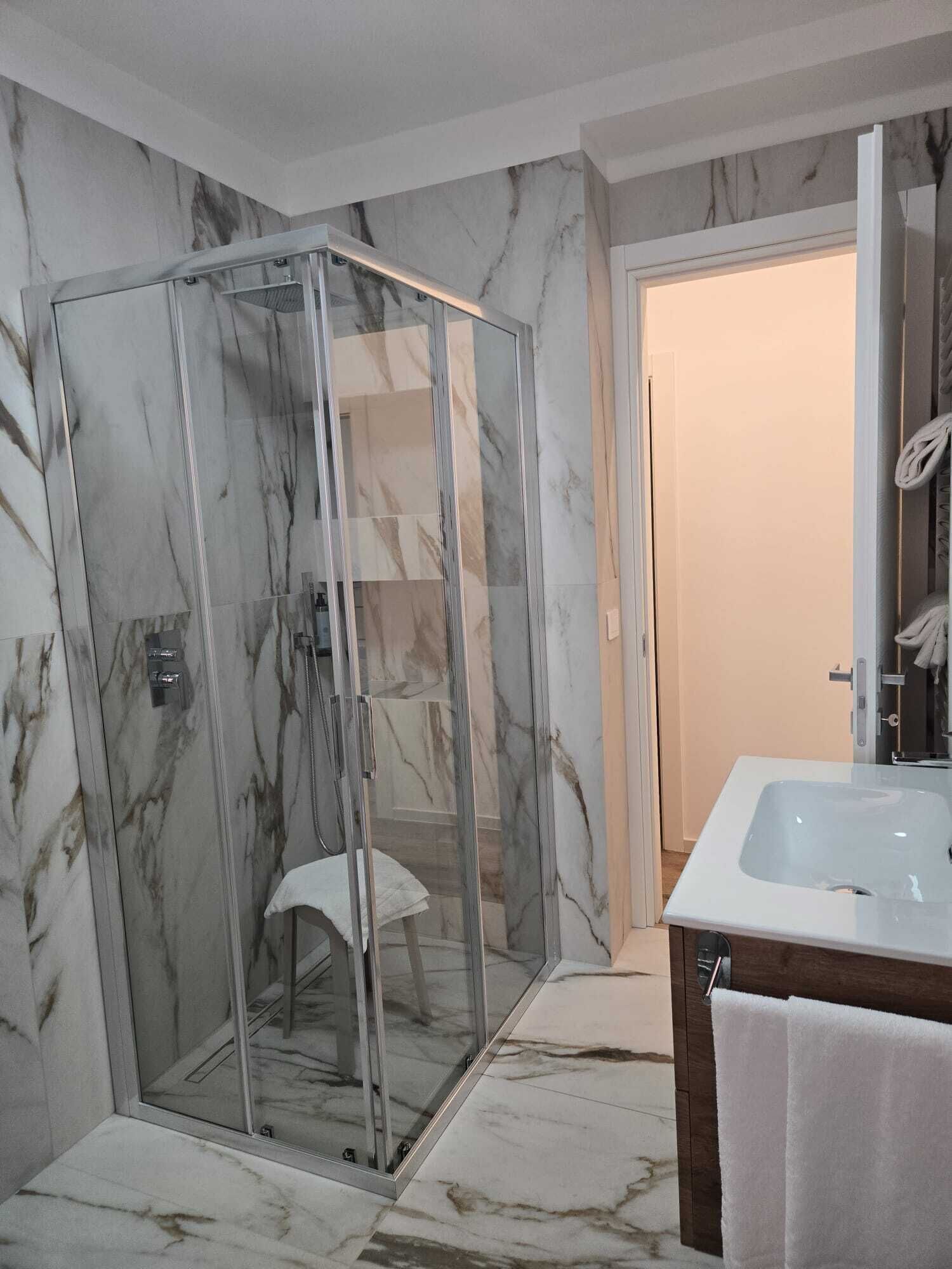 Un bagno moderno con doccia vetrata, pavimento in marmo e lavandino bianco con piano in legno.