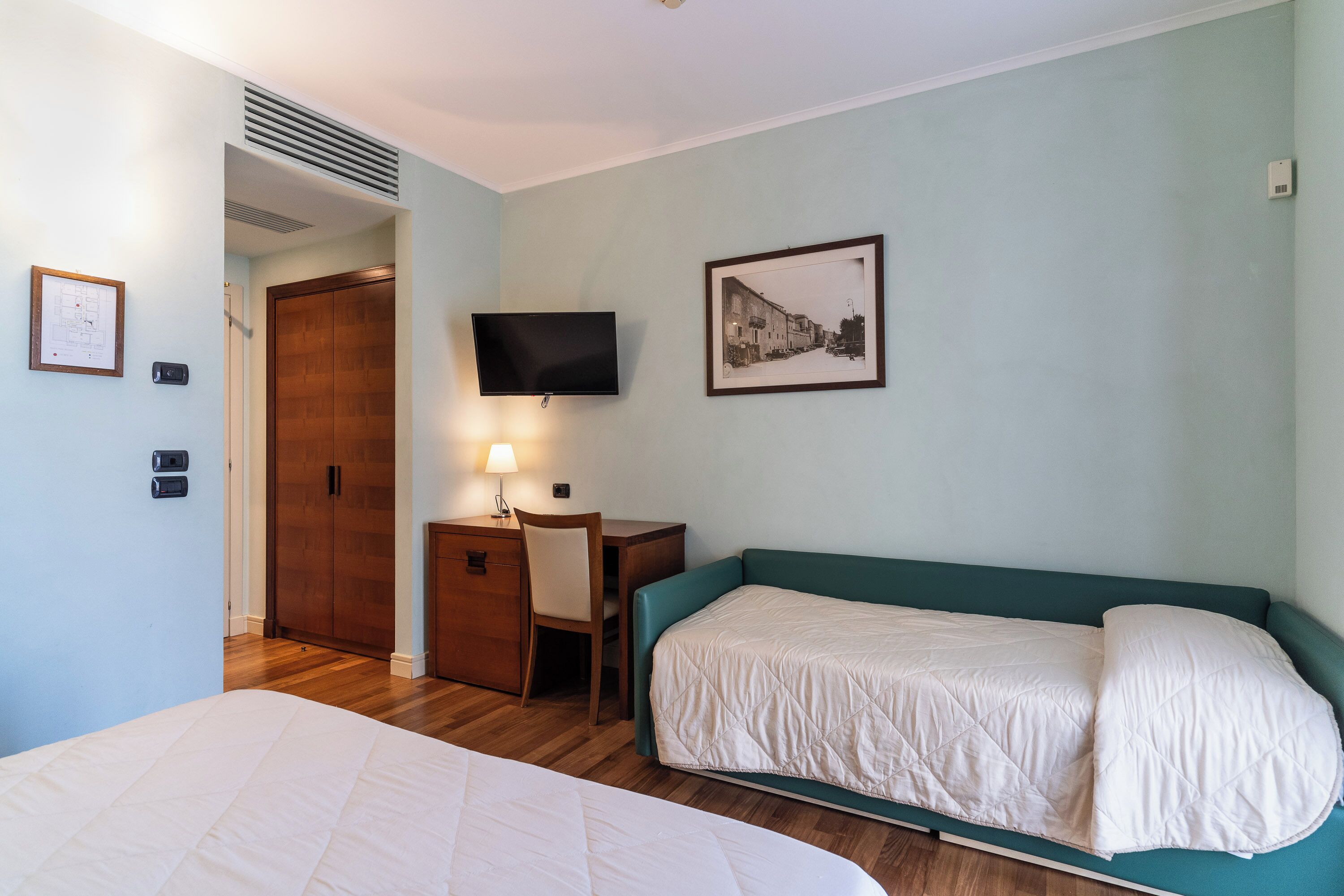 Ein Schlafzimmer mit einem Bett, einem Schreibtisch, einem Stuhl, einem Fernseher und einer Tür.