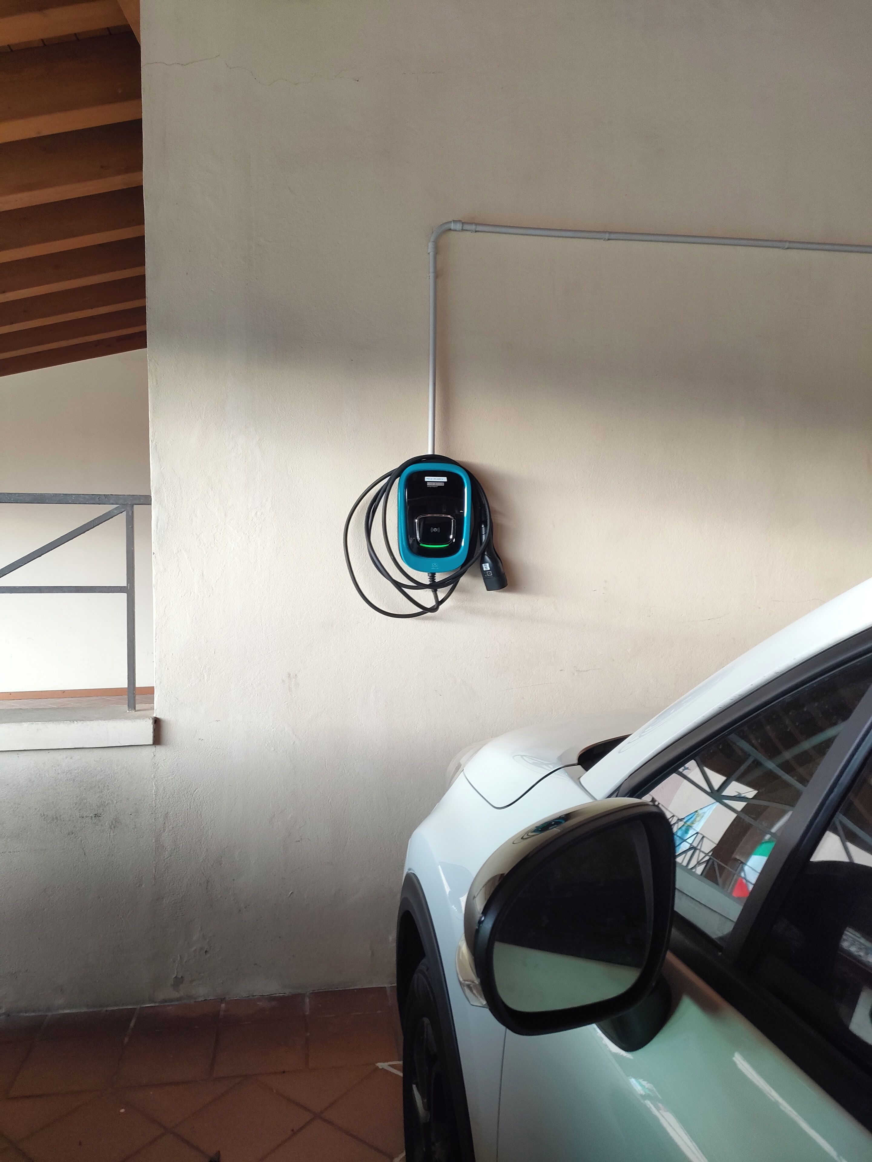 Un'auto bianca parcheggiata all'interno con una stazione di ricarica elettrica montata a parete.