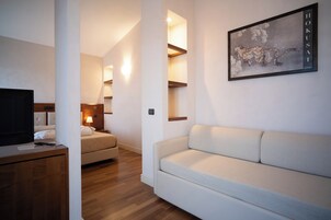 A modern hotel room with a sofa, a bed, a TV, and a wall-mounted artwork.
