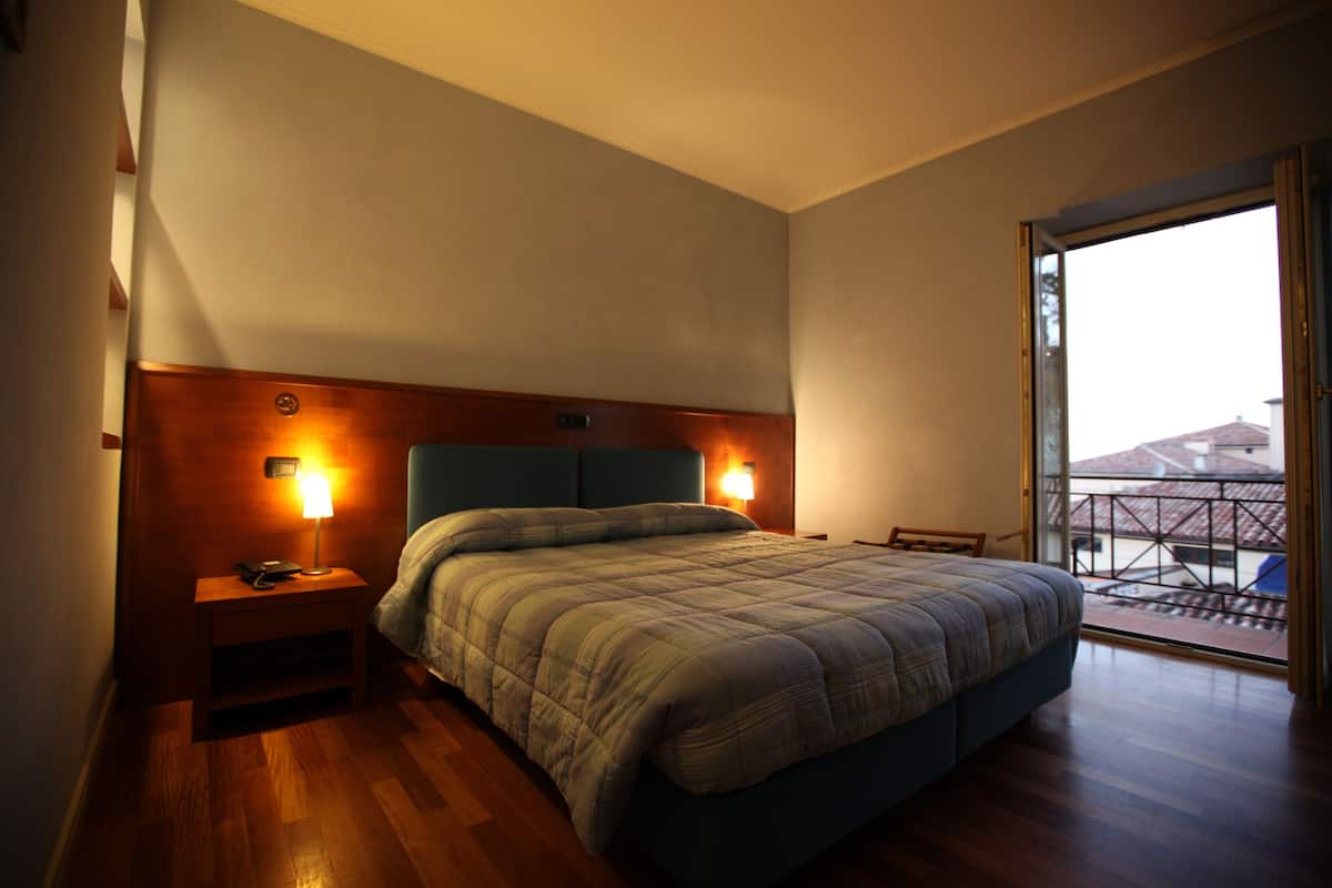 A bedroom with a large bed, wooden headboard, bedside lamps, and a view through a sliding glass door to an outdoor balcony.
