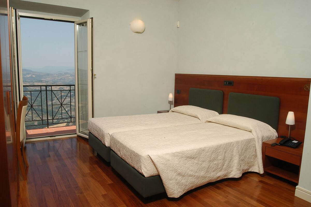 A bedroom with a bed, bedside tables, and a view through a glass door.