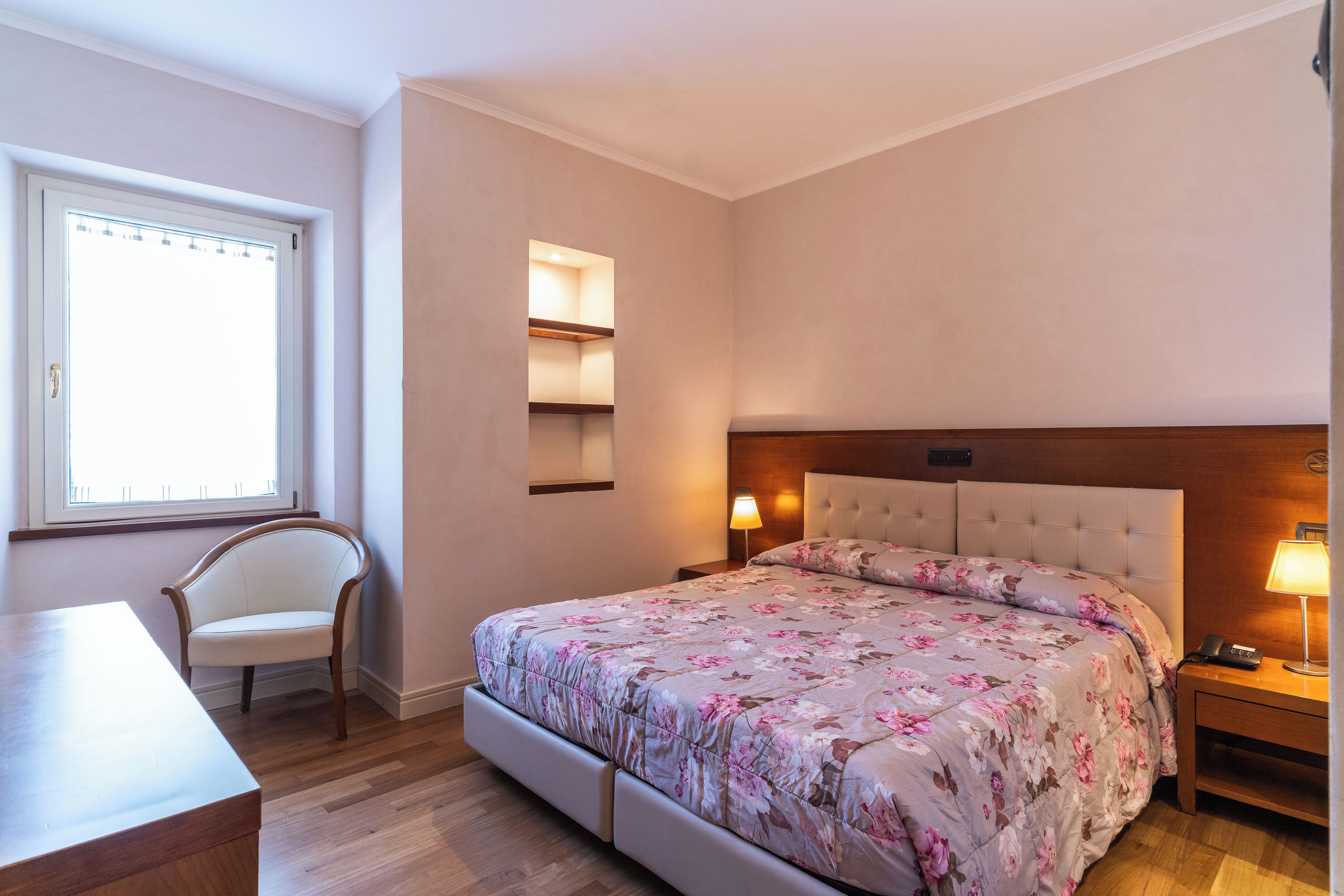 A bedroom with a large bed, a chair, a bedside table, and a window.