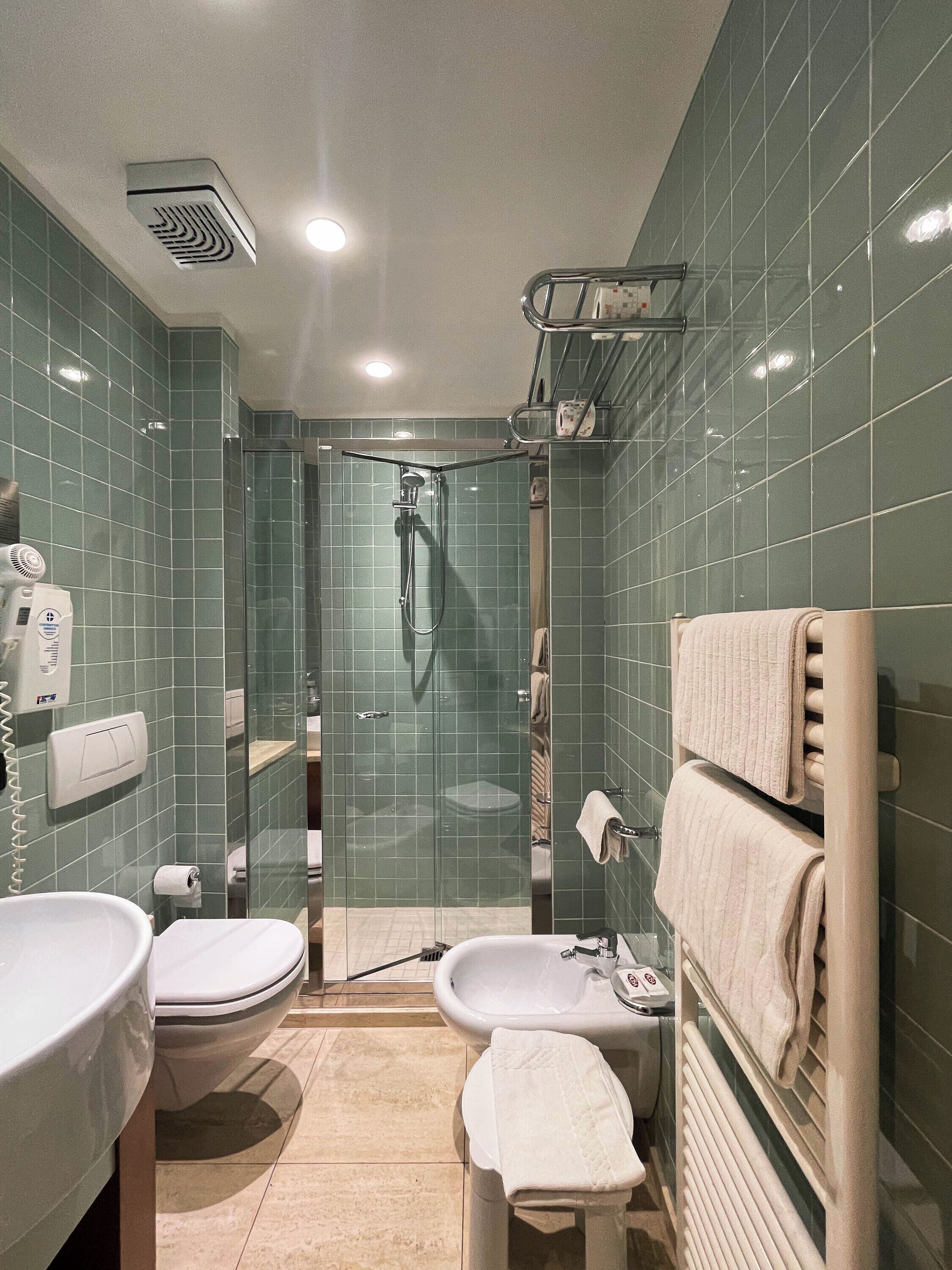 Un baño moderno con ducha de vidrio, inodoro, lavamanos y toallero.