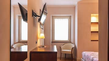 A hotel room with a wooden desk, a chair, a bed, a large mirror, and a window with blinds.
