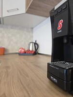 Una cocina con cafetera, hervidor y una bandeja de sobres rojos.