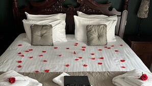 A neatly made bed with rose petals, towels, and a remote control on a textured bedspread.