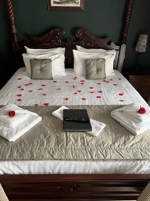 A neatly made bed with rose petals, towels, and a remote control on a textured bedspread.