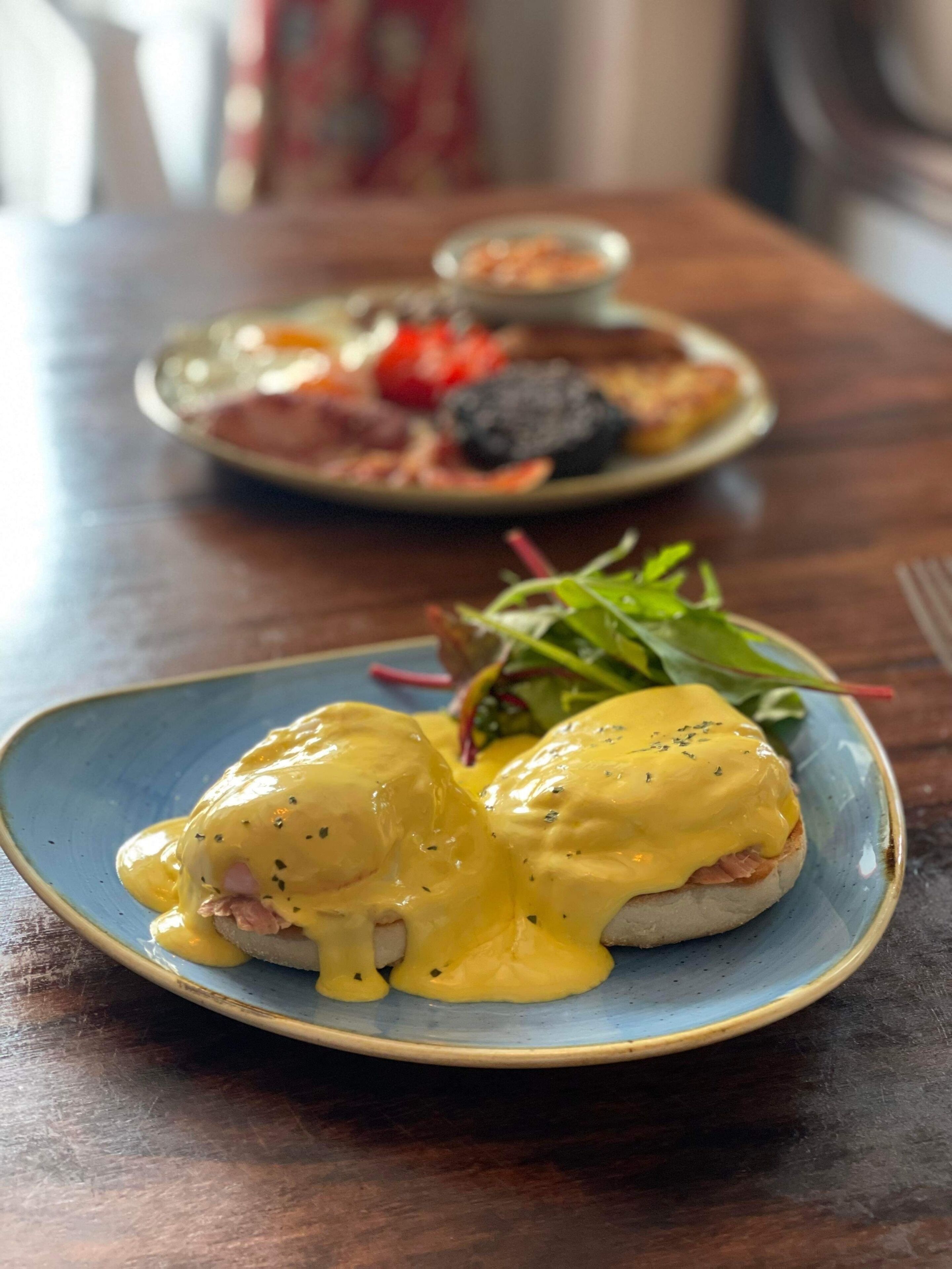 A plate of eggs benedict with hollandaise sauce on a blue plate.