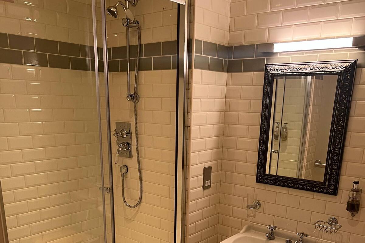 A bathroom with a glass-enclosed shower, a white sink, and a mirror with an ornate frame.