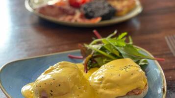 Un plato de huevos benedictinos con salsa holandesa sobre un plato azul.