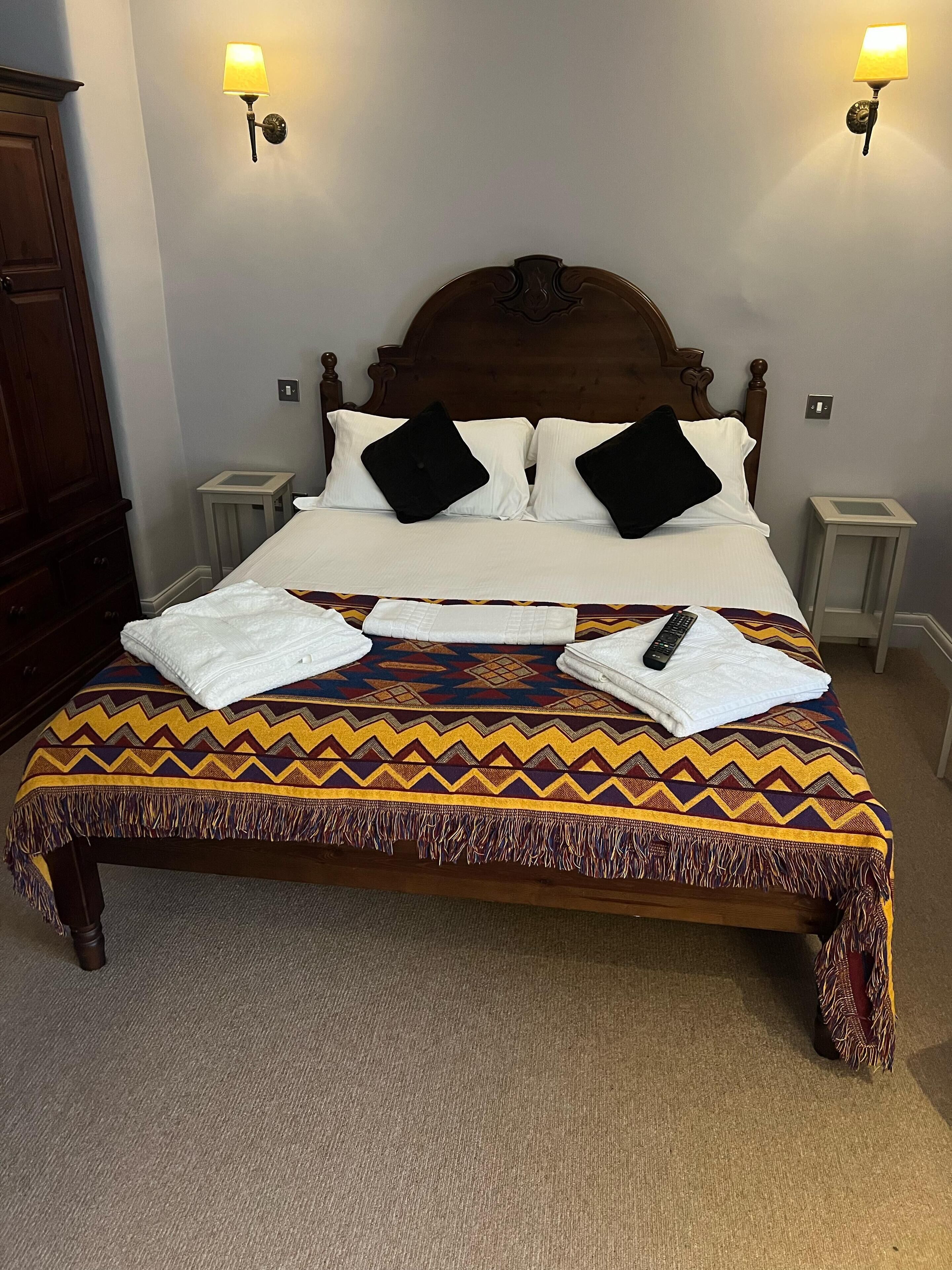 Een net opgemaakt bed met een bedsprei met dessin, twee bedlampen en een houten hoofdeinde.
