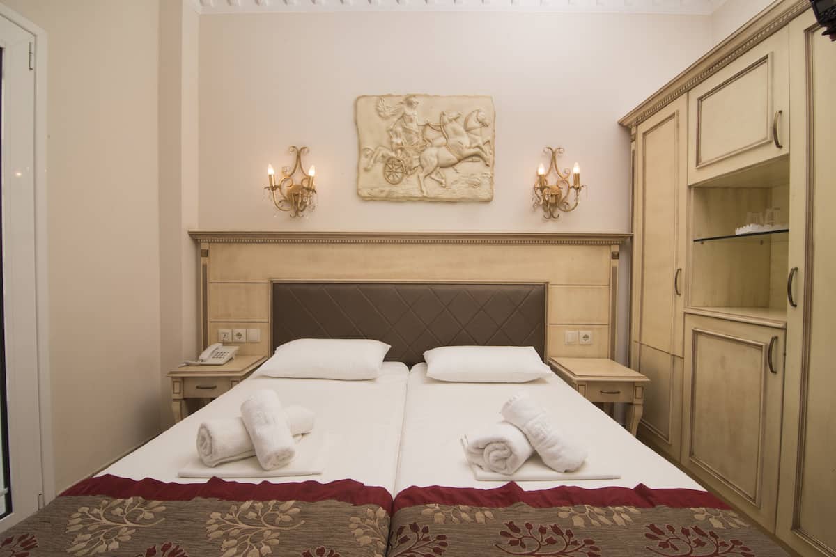 Cama de casal com roupa de cama e toalhas brancas, cabeceira de madeira, mesas de cabeceira com luminárias e uma obra de arte pendurada na parede.