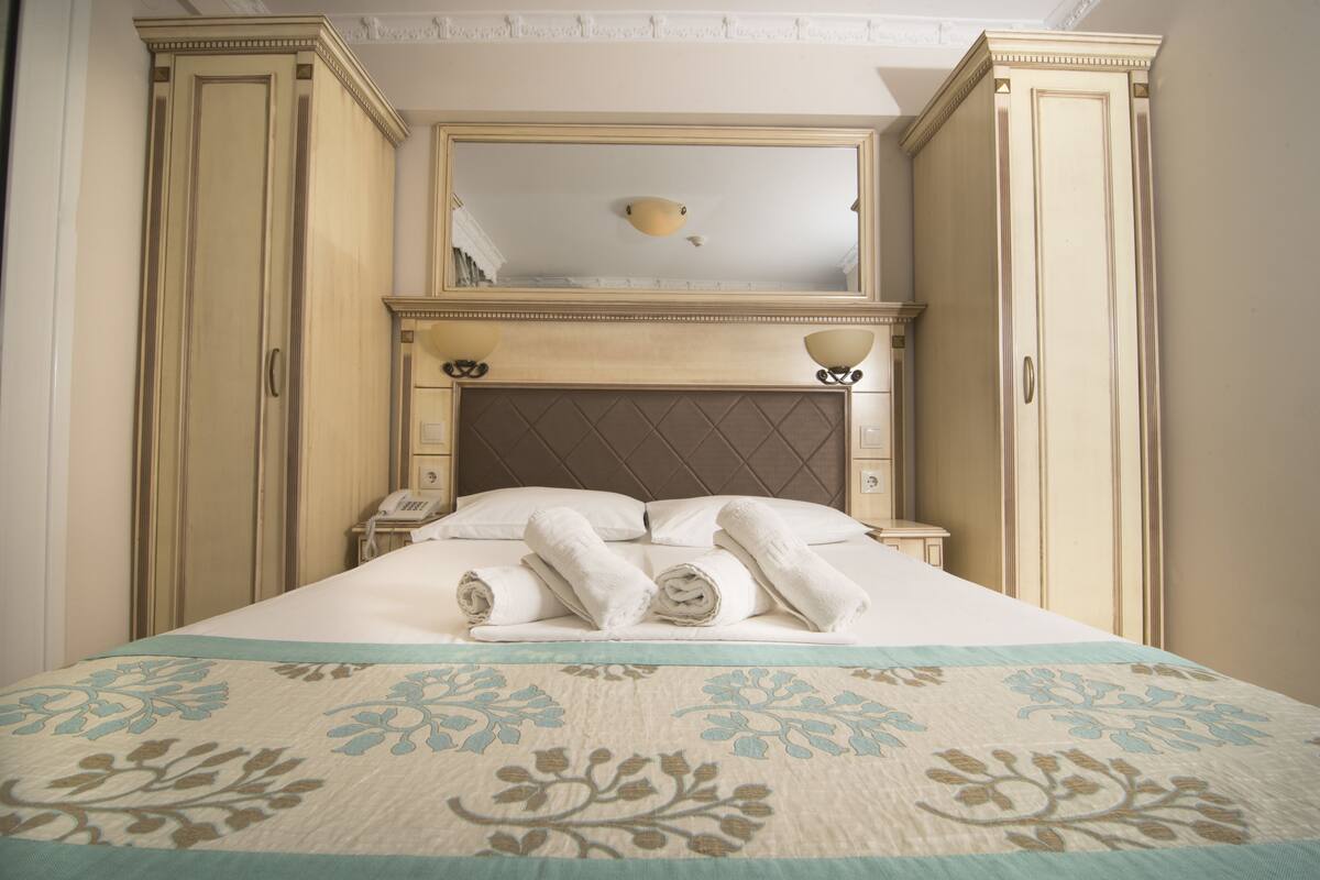Uma cama bem arrumada com toalhas enroladas, uma mesa de cabeceira com telefone e um espelho sobre a cama.