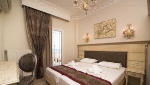 A hotel room with a bed, a chair, a desk, and a view of the city through a window. - Parthenon Art Hotel (Katerini)