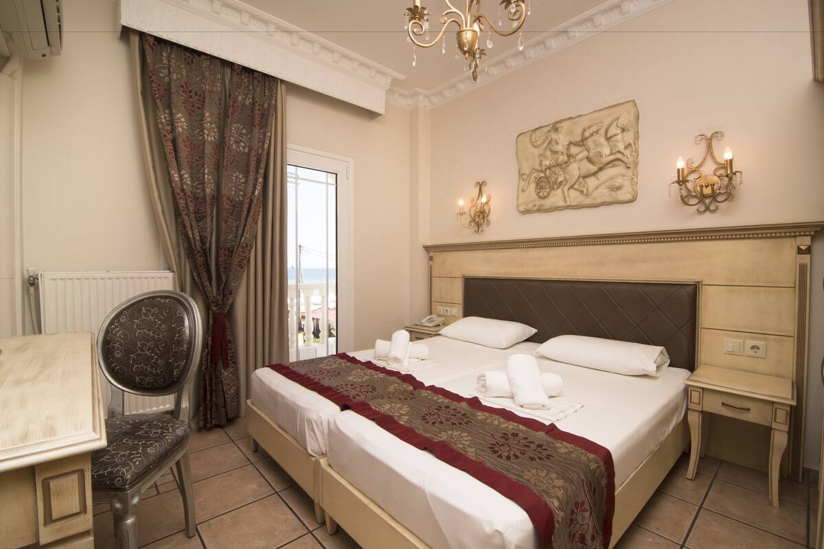 Quarto de hotel com cama, uma cadeira, escrivaninha e vista para a cidade pela janela.