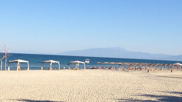 A beach with multiple sun umbrellas and beach chairs, a clear sky, and a mountain in the background. - Parthenon Art Hotel (Katerini)