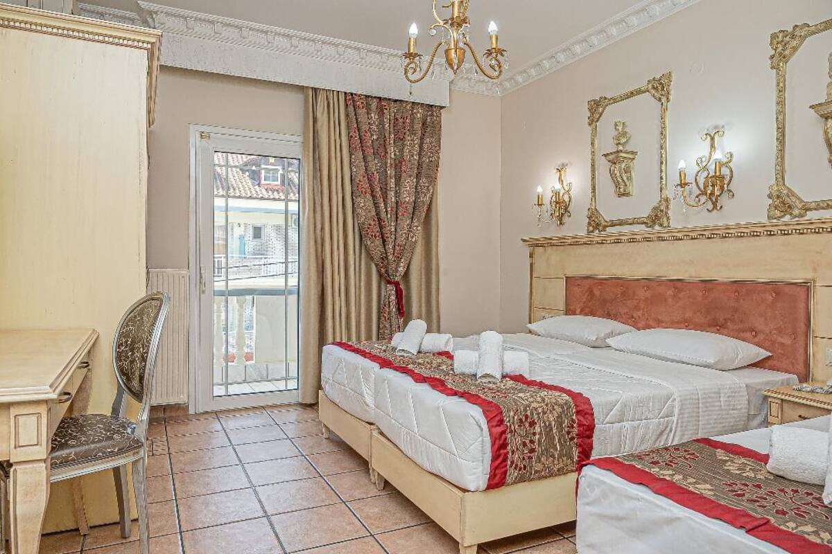 Quarto de hotel com uma cama grande, uma escrivaninha, uma cadeira e uma varanda com cortinas.