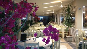 A restaurant with tables and chairs, a ceiling fan, and potted plants. - Parthenon Art Hotel (Katerini)