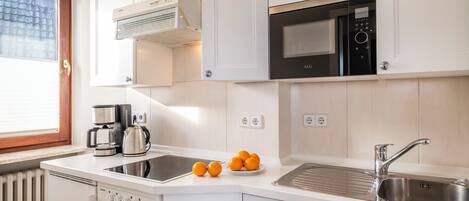 A modern kitchen with white cabinetry, a built-in oven, microwave, and dishwasher. There are oranges on the counter and a coffee maker.