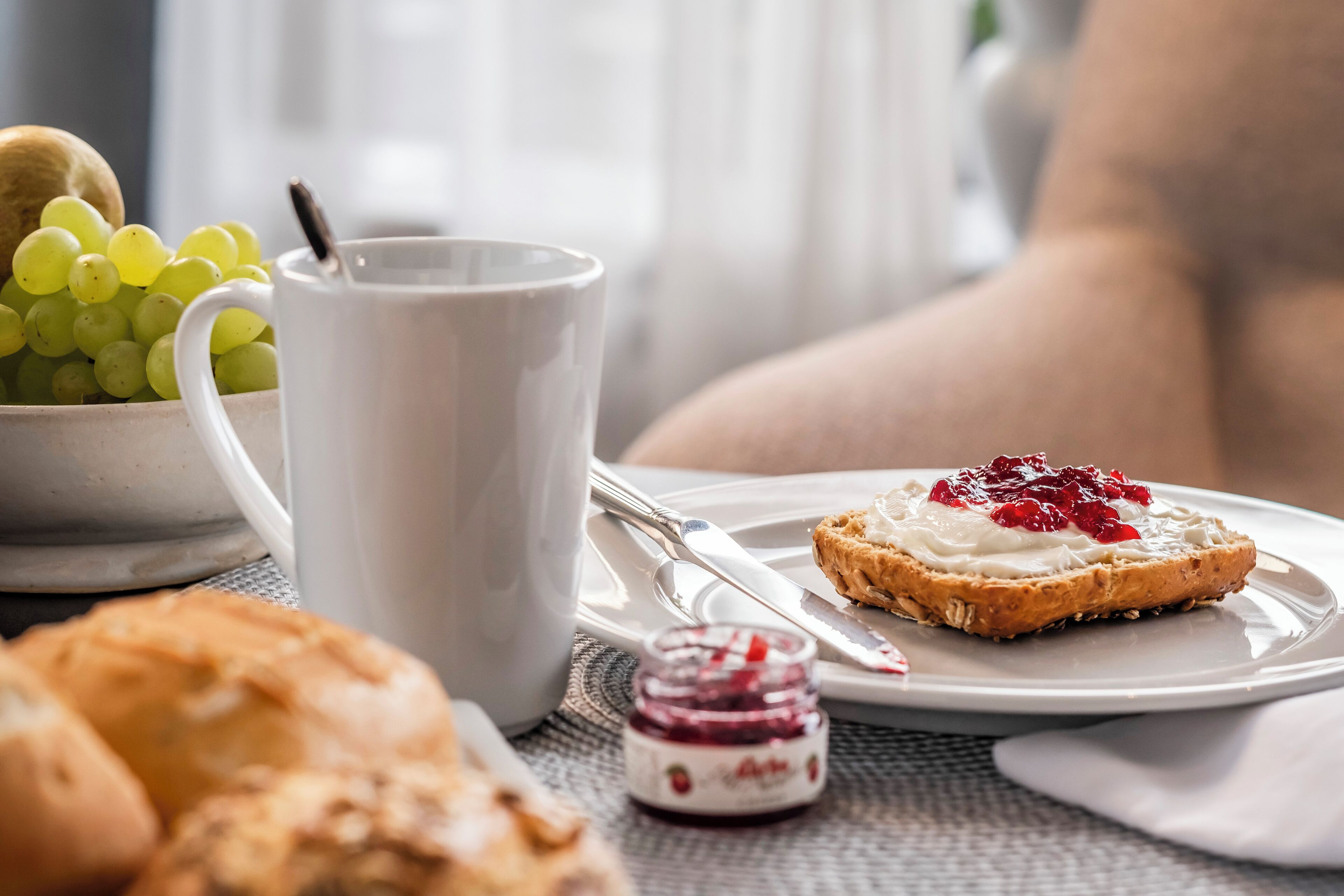 En frukostuppsättning med en tallrik rostat bröd, en skål med vindruvor, en mugg och en liten burk marmelad.