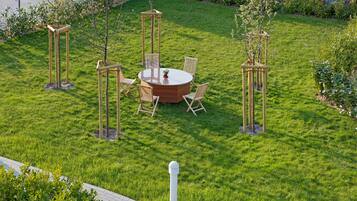 A well-maintained outdoor seating area with a round table and chairs, surrounded by small trees and a grassy lawn.