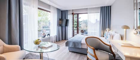 Ein modernes Hotelzimmer mit Glastisch, einer Couch, einem Schreibtisch mit Lampe, einem Bett und einem Fernseher.