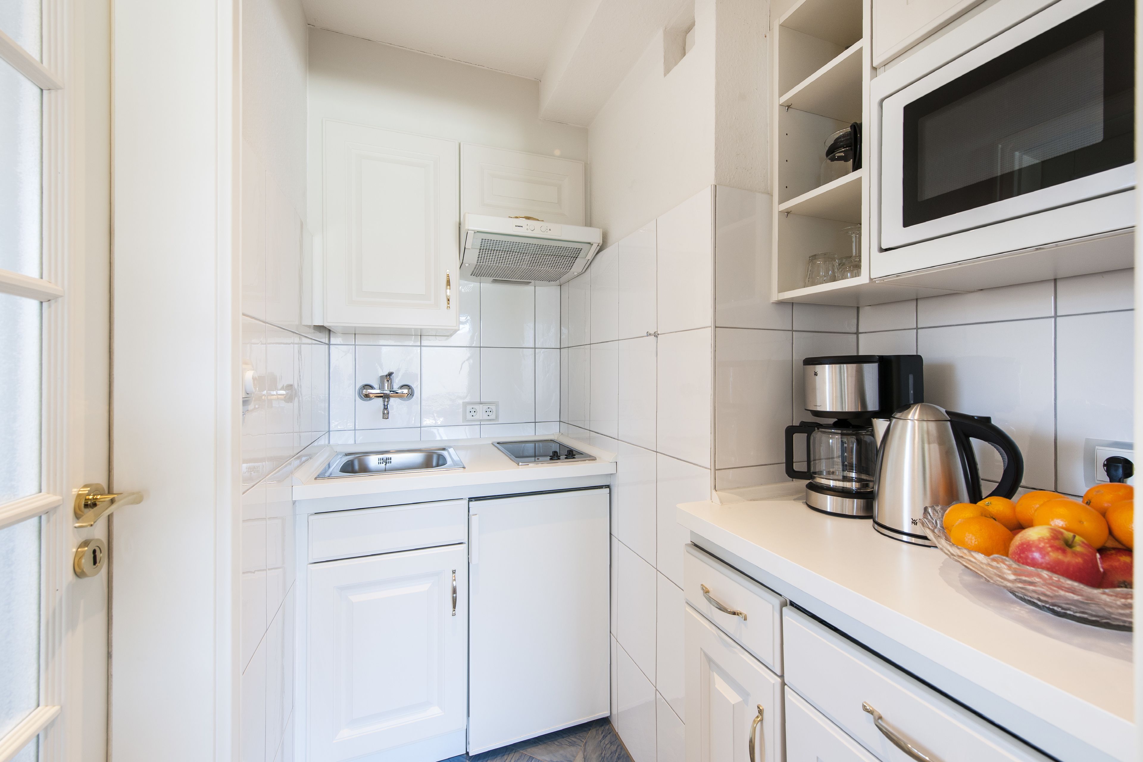 A compact kitchen with white cabinets, a microwave, a coffee maker, and a fruit bowl.