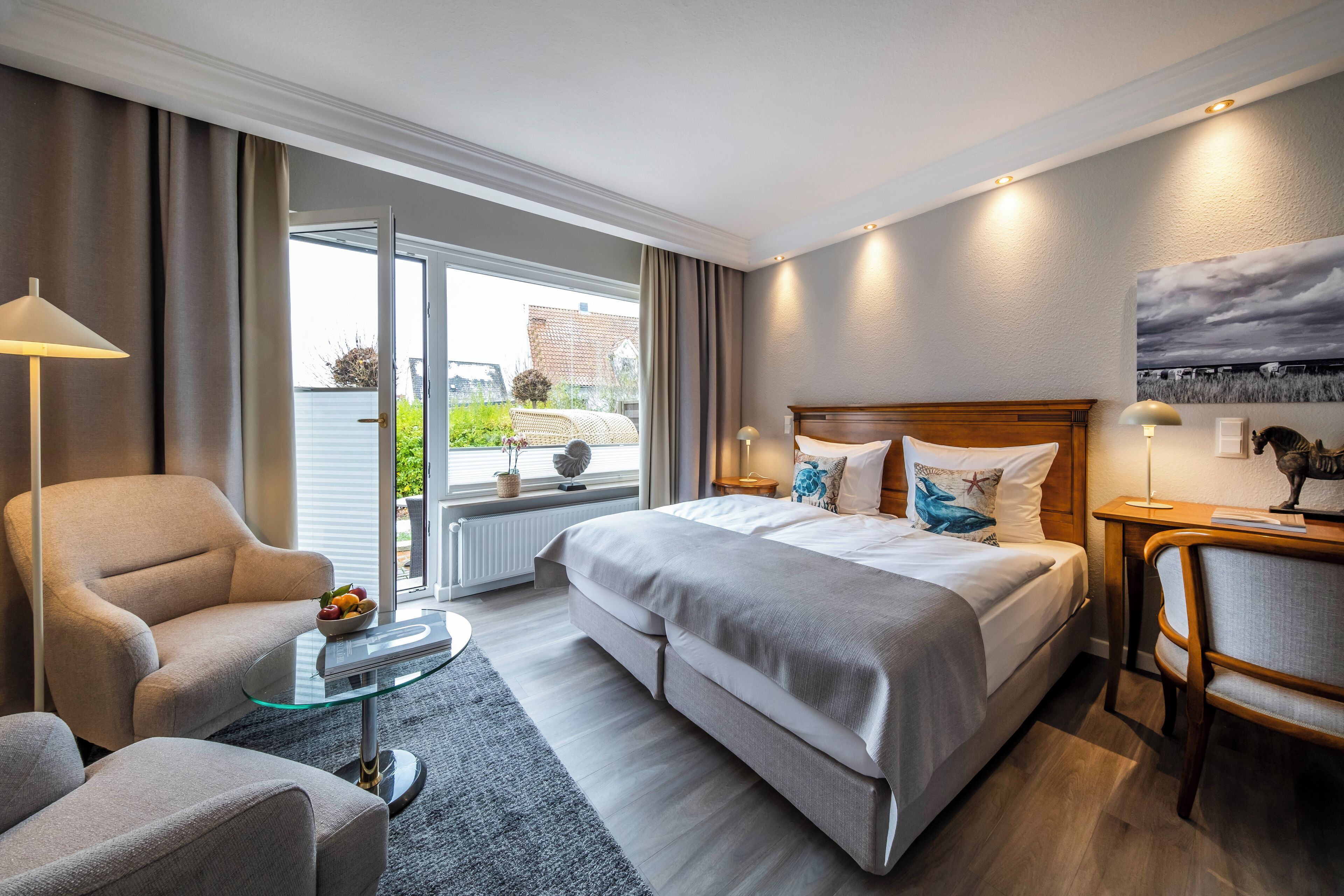 A modern hotel room with a large bed, a sitting area with a glass coffee table, and a view through the glass door.