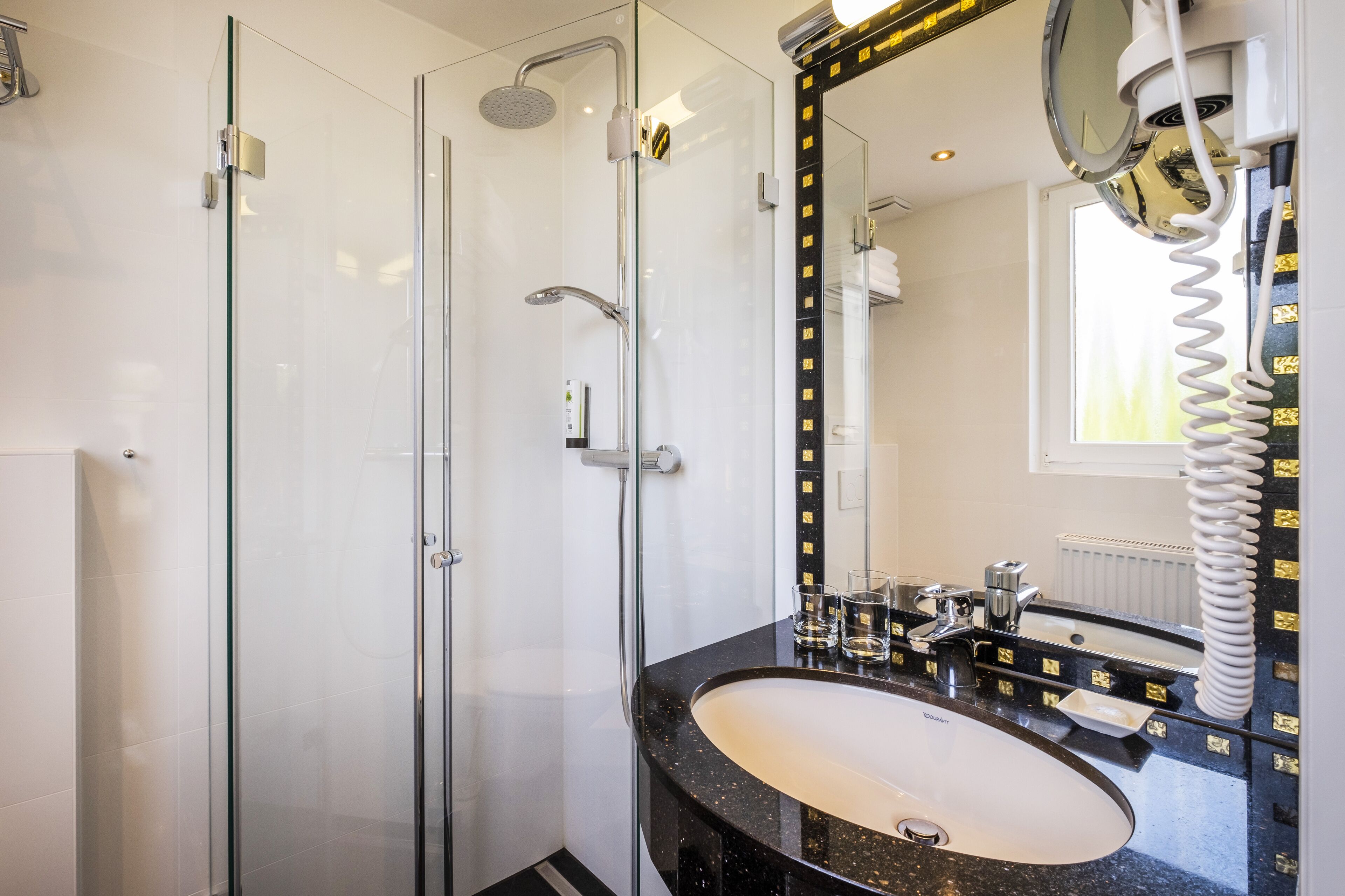A modern bathroom with a glass-enclosed shower, a black marble sink, and a large mirror with a gold frame.
