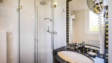 A modern bathroom with a glass-enclosed shower, a black marble sink, and a large mirror with a gold frame.